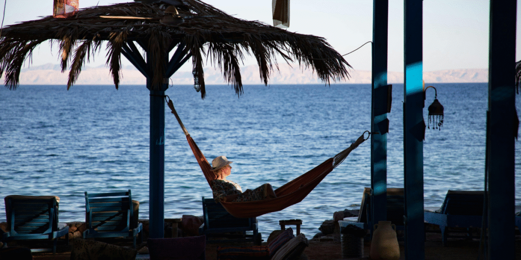 A traveller enjoying peaceful coastal views laying on a hammock during an off-peak travel getaway.