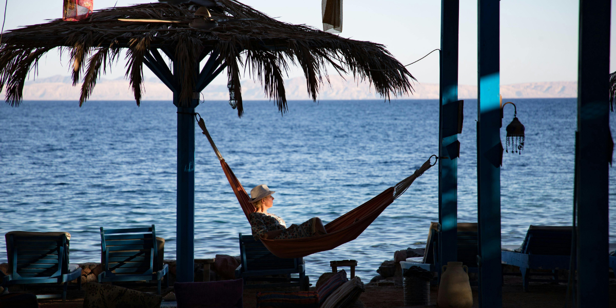 A traveller enjoying peaceful coastal views laying on a hammock during an off-peak travel getaway.